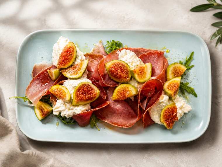 Culatello con burrata, fichi freschi e rucola su un piatto azzurro